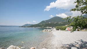 A pebble beach with clear water, a rocky shoreline, and a mountainous backdrop. - Julia s House With Lakeview (Toscolano Maderno)