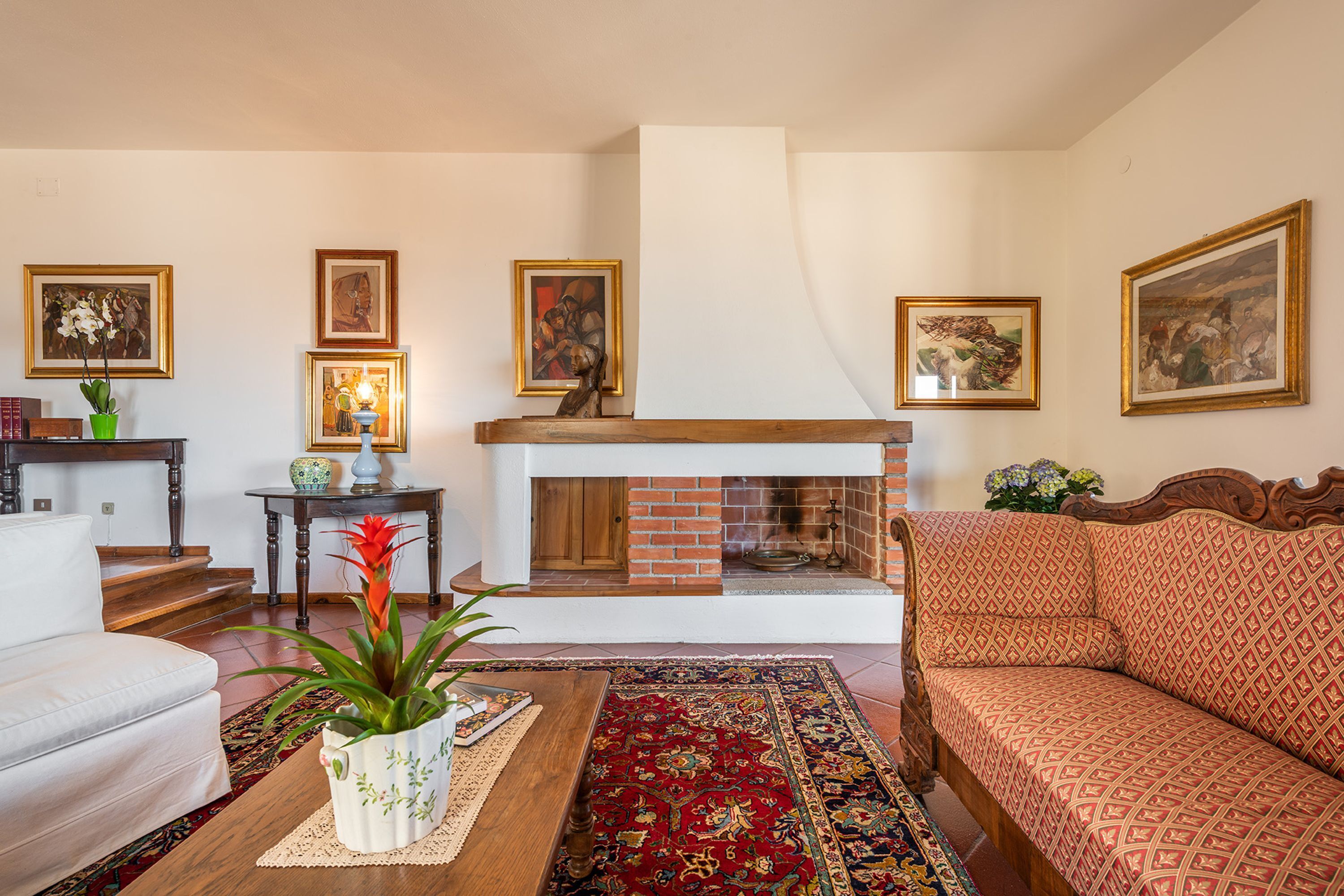 A living room with a fireplace, a sofa, a coffee table with a plant, and a patterned rug.