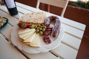 Un plato de comida con queso, aceitunas, salchichón en rodajas y una fresa sobre una mesa blanca.