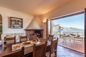 Un comedor con chimenea de ladrillo, una mesa lista para cuatro comensales y vistas a las montañas a través de amplios ventanales.
