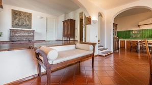 A spacious living area with a wooden bench, a dining table with chairs, and a kitchen with green tiles. - Villa Ruju in Dorgali (Dorgali)