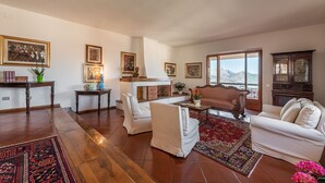 A spacious living room with a fireplace, white furniture, and a large window offering a mountain view. - Villa Ruju in Dorgali (Dorgali)