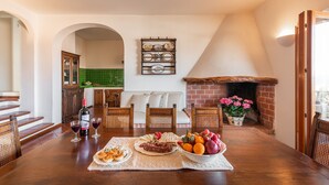 A dining area with a wooden table set for a meal, a fireplace, and a green-tiled backsplash in the background. - Villa Ruju in Dorgali (Dorgali)