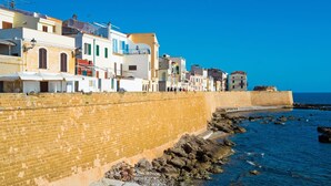 A coastal town with a stone wall, buildings with balconies, and a clear blue sky. - Bilo Agostino 2 in Alghero (Alghero)