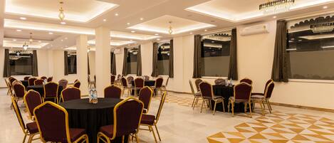 A spacious banquet hall with round tables and chairs, recessed lighting, and a patterned floor.