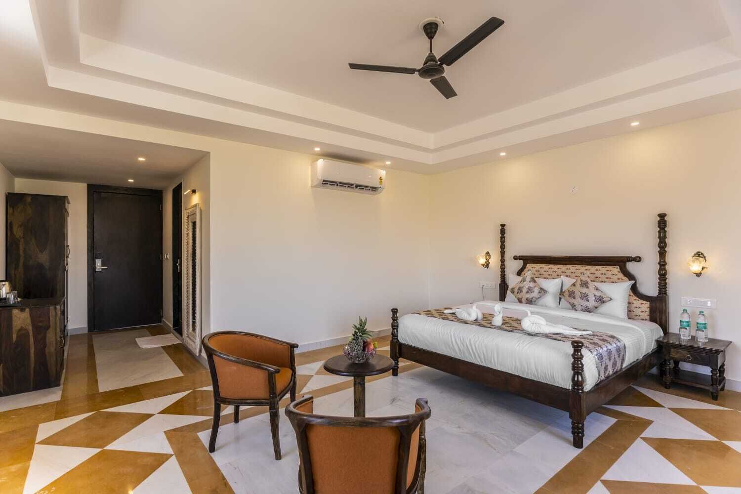 Una camera d'albergo con un letto grande, un ventilatore a soffitto, un tavolino con sedie e un centrotavola decorativo a forma di ananas.
