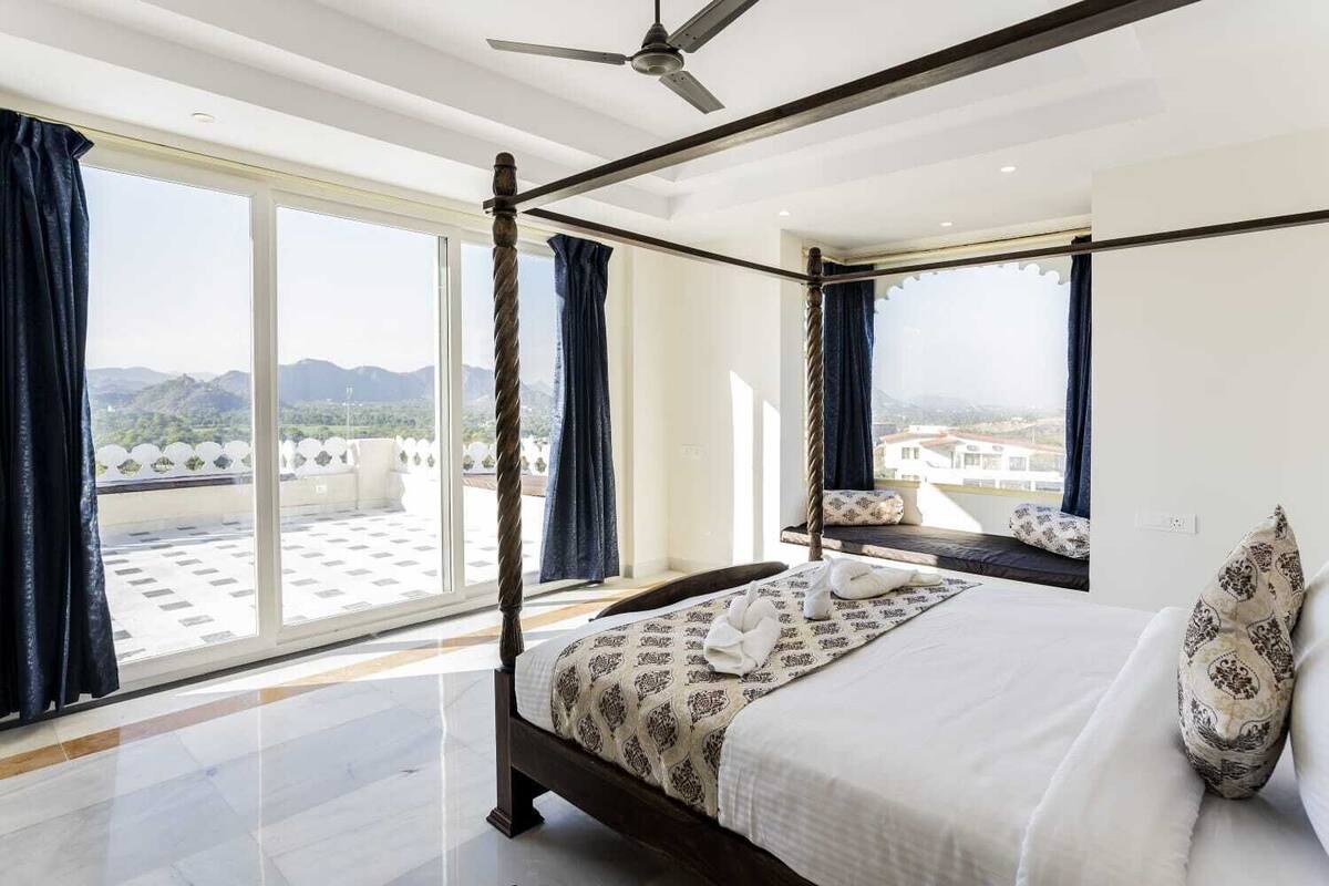 Una cama con dosel con vistas a la ciudad y a las montañas a través de amplias ventanas.