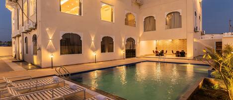 A poolside area with lounge chairs, a swimming pool, and a building with multiple windows and balconies.
