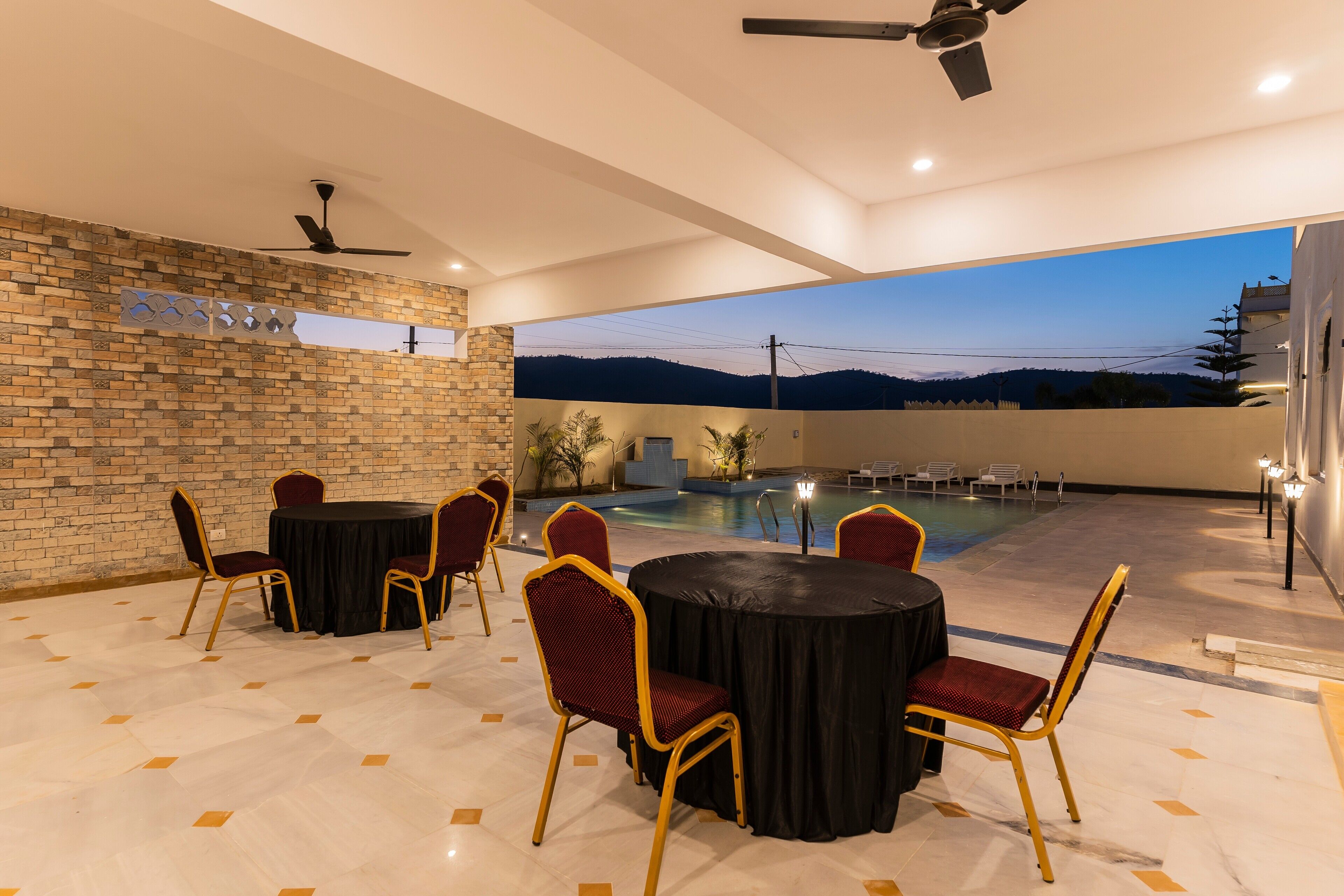 An outdoor patio with a pool, a brick wall, and a view of the mountains at dusk.