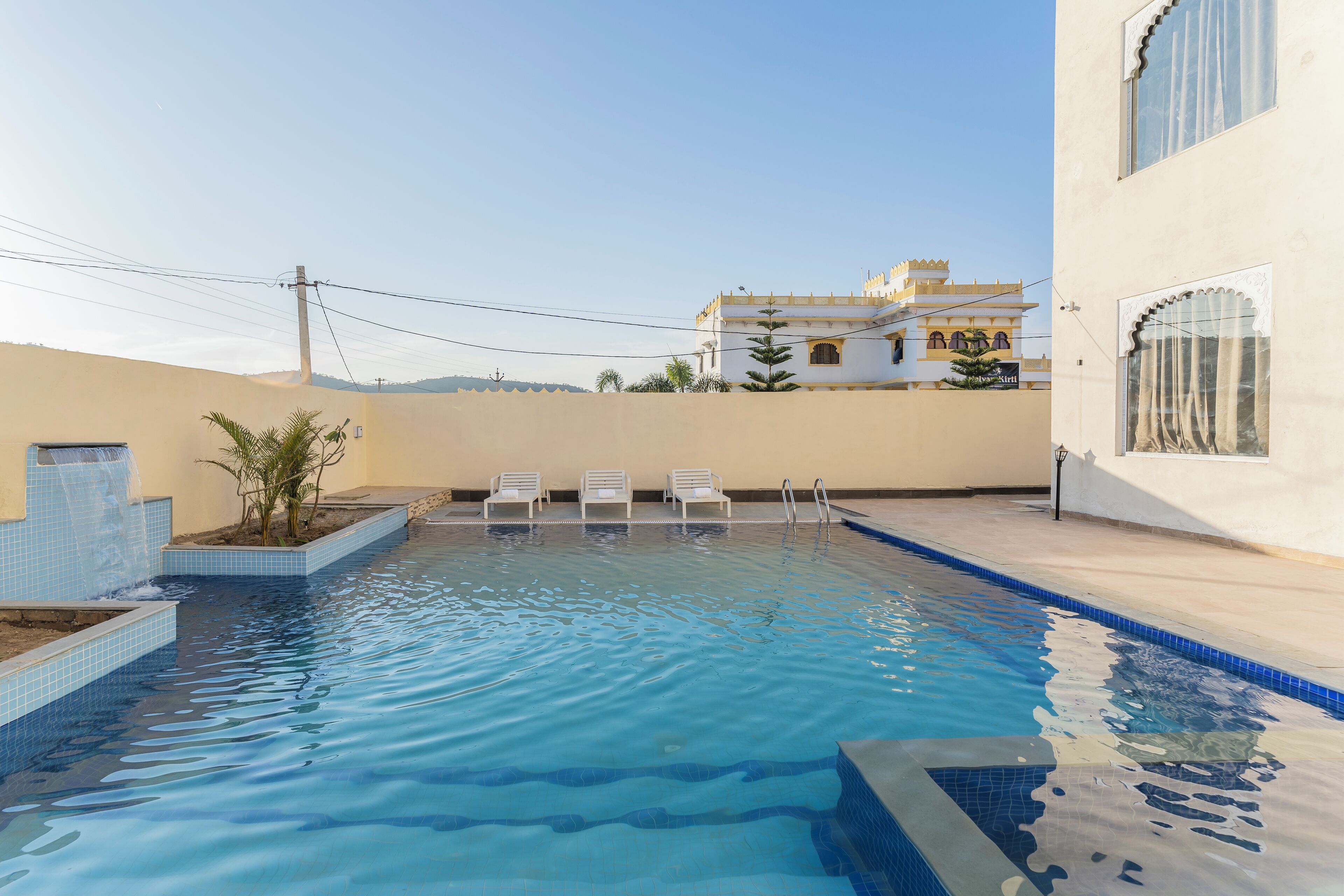 Una piscina con agua cristalina azul, rodeada por un muro bajo y algunas sillas de descanso.
