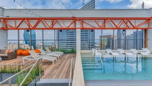 A rooftop pool area with lounge chairs and a seating area, large windows offering city views. - Stunning CozySuites on Elm St. 11 (Dallas)