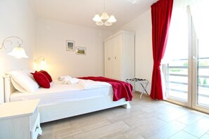 Una camera da letto con un letto, pareti bianche, un armadio, una finestra con tende rosse e una lampada a soffitto.