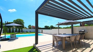 Eine überdachte Terrasse mit Pool, Sitzgelegenheiten im Freien und einer Grillzone.