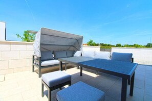 Un patio esterno con zona salotto coperta, un tavolo e una panchina.