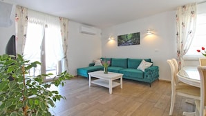 Ein Wohnzimmer mit einem salbeigrünem Sofa, einem weißen Couchtisch und einem Essbereich mit weißem Tisch und Stühlen.