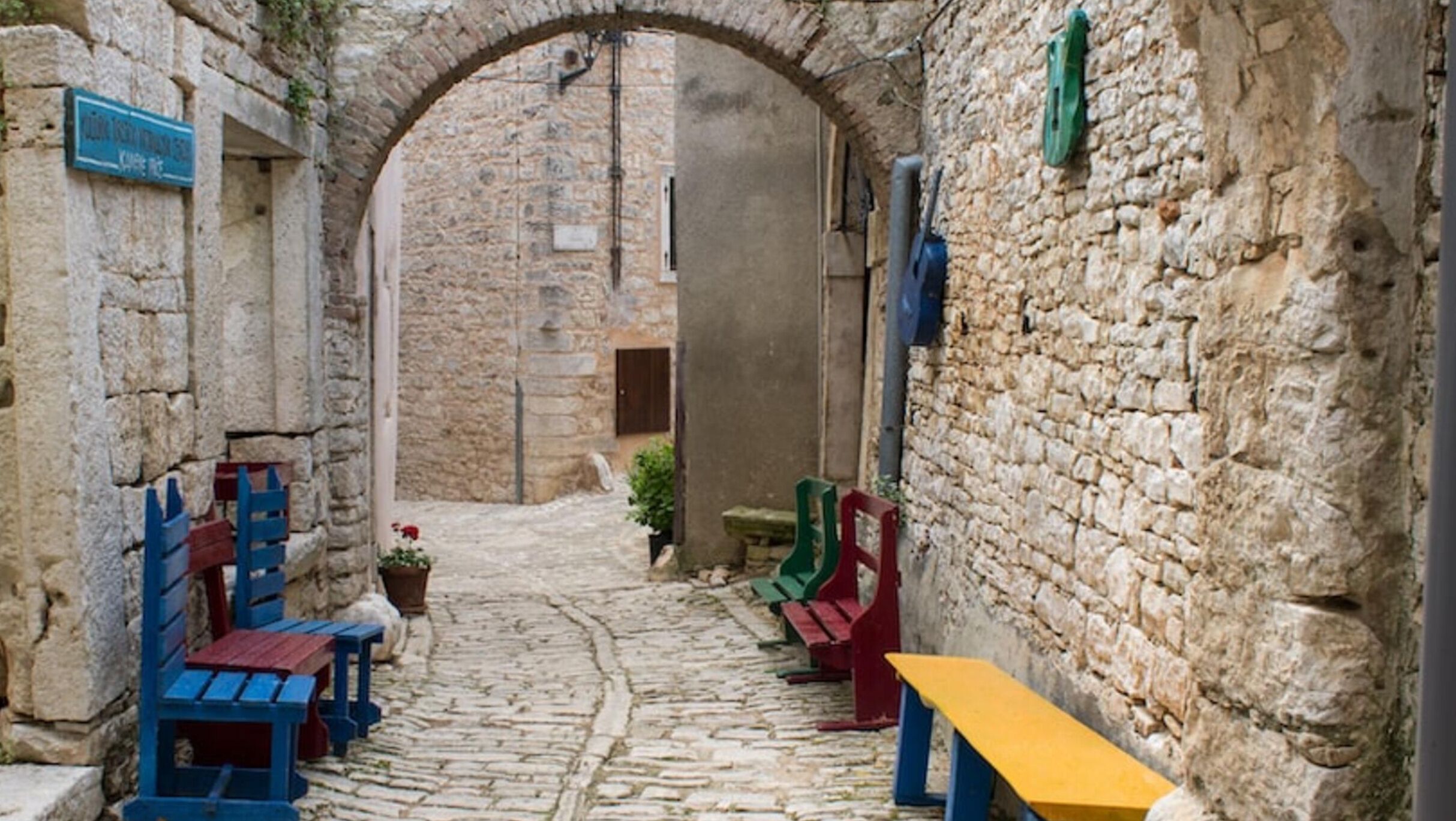 A narrow cobblestone street with stone walls, benches, and a sign.