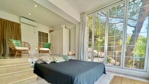 A bedroom with a large bed, a chair, a small table, and a view of the outdoors through a sliding glass door. - P67- Playetas- ServHouse (Oropesa)
