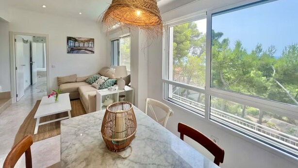 A modern living room with a large window, a dining area, and a cozy seating area. - P67- Playetas- ServHouse (Oropesa)