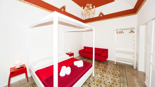 A room with a four-poster bed, red sofa, and a wardrobe. - Visitsicilia Donn Anna 2 (Castellammare del Golfo)