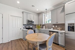 A modern kitchen with white cabinets, stainless steel appliances, and a wooden dining table with chairs.