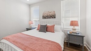 Une chambre à coucher comprenant un lit, deux tables de chevet, un ventilateur de plafond et un tableau accroché au mur.