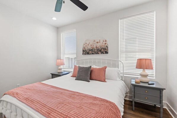 A bedroom with a bed, two bedside tables, a ceiling fan, and a wall-mounted painting.