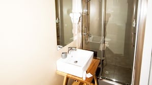 A modern bathroom with a glass-enclosed shower, a sink with a wooden vanity, and patterned floor tiles. - Visitsicilia Donn Anna (Castellammare del Golfo)