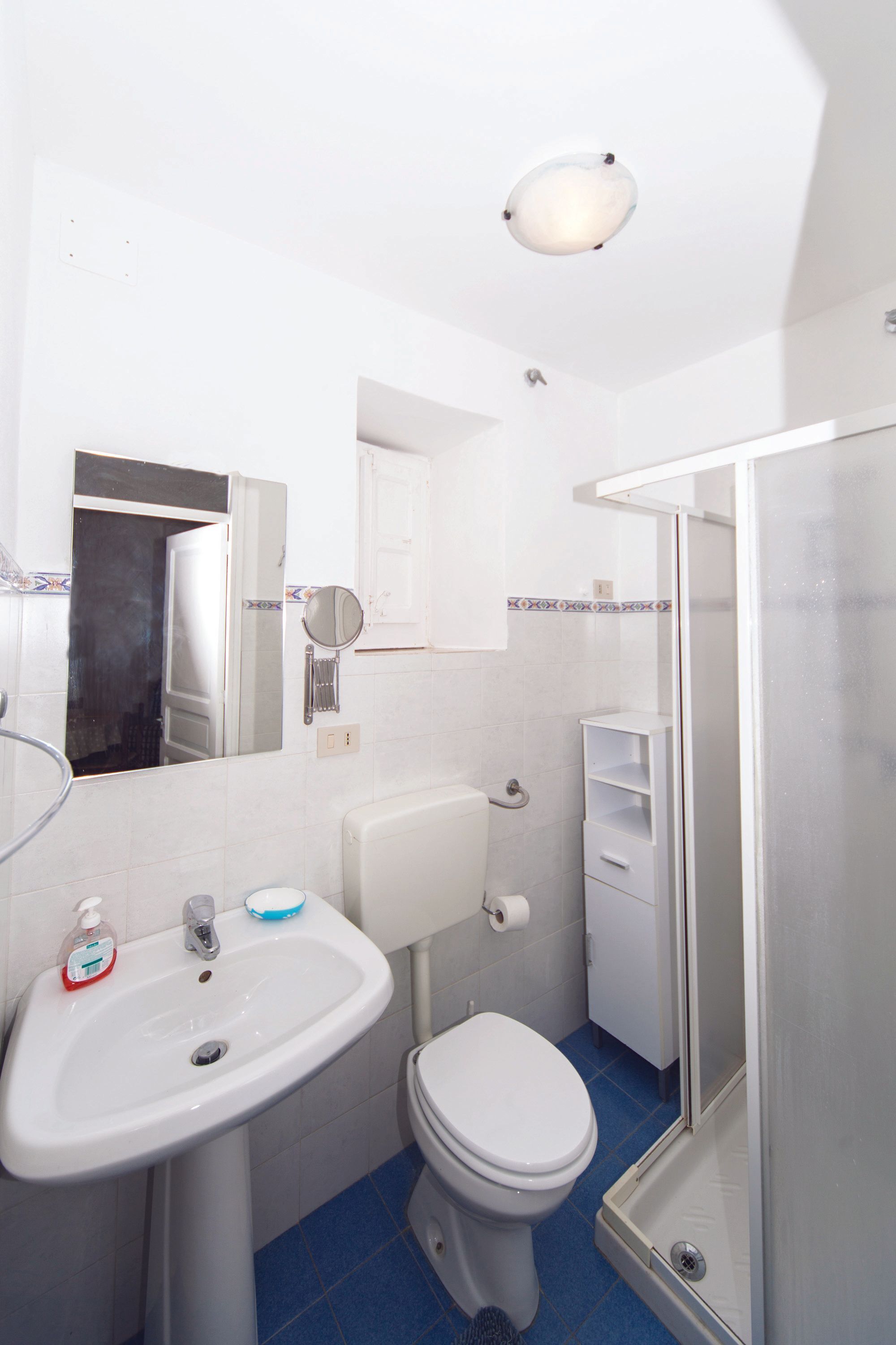 Une salle de bain avec un lavabo blanc, des toilettes et une douche fermée par une paroi de verre.