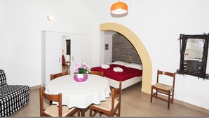 A room with a round dining table, two wooden chairs, a bed with a red blanket, and a small wooden chair. - Visitsicilia Donn Anna (Castellammare del Golfo)
