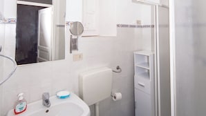 Un baño con lavamanos blanco, inodoro y ducha con mampara de vidrio.
