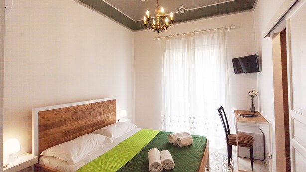 Ein Hotelzimmer mit einem Bett mit Holz-Kopfteil, einer grünen Tagesdecke, zwei aufgerollten Handtüchern, einem Schreibtisch mit Fernseher und einem Sessel.