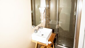 Ein modernes Badezimmer mit einer gläsernen Duschkabine, einem Holztischchen und einem gemusterten Boden.