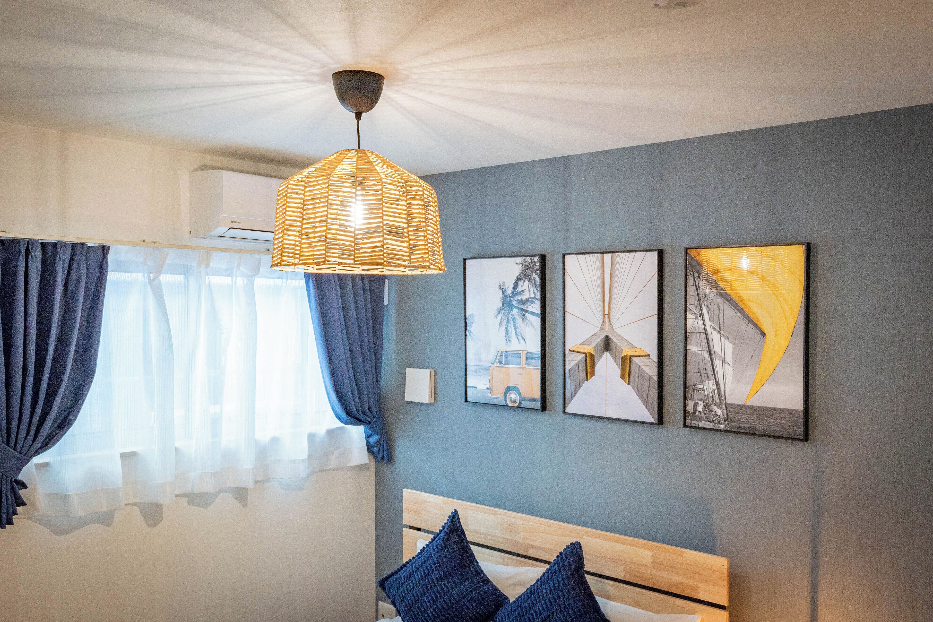 A bedroom with a bed, a hanging light fixture, and three framed pictures on the wall.