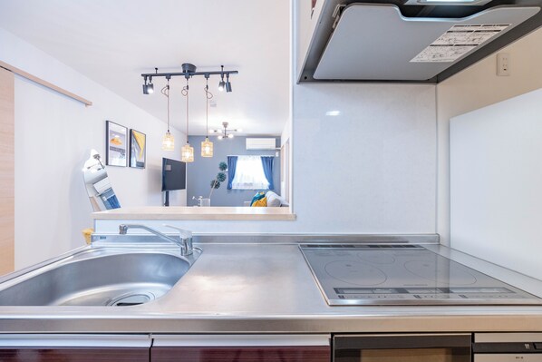 Une cuisine moderne dotée d’un évier en acier inoxydable, d’une cuisinière encastrée, de luminaires suspendus et d’œuvres d’art encadrées accrochées au mur.