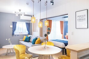 A modern living room with a sofa, yellow chairs, a round table, and a kitchen area. - Plandor hanazono (Osaka)