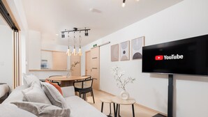 Un soggiorno moderno con una TV a schermo piatto, un'area pranzo con tavolo e sedie in legno, e una cucina sullo sfondo.
