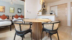Una moderna camera d'albergo con zona pranzo, un tavolo rotondo in legno e sedie nere con sedili intrecciati.