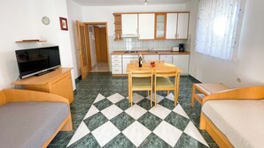Een kleine kamer met een bed, een televisie, een eettafel met stoelen, een kitchenette en een badkamer.