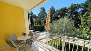 Een balkon met een tafel en stoelen, een zwembad en omliggend groen.