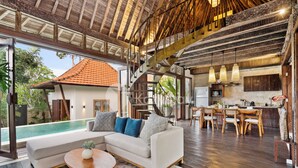 A spacious living area with a large sofa, a dining table, and a staircase leading to an upper level.