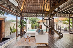 A spacious living area with a wooden ceiling, a white sofa, a small table, and a staircase leading to an outdoor area. - Dewandaru Villa by Kozystay - Canggu (Canggu)