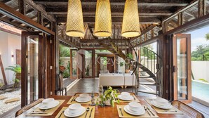 A dining area with a wooden table set for four, surrounded by large windows and a staircase leading to an upper level.