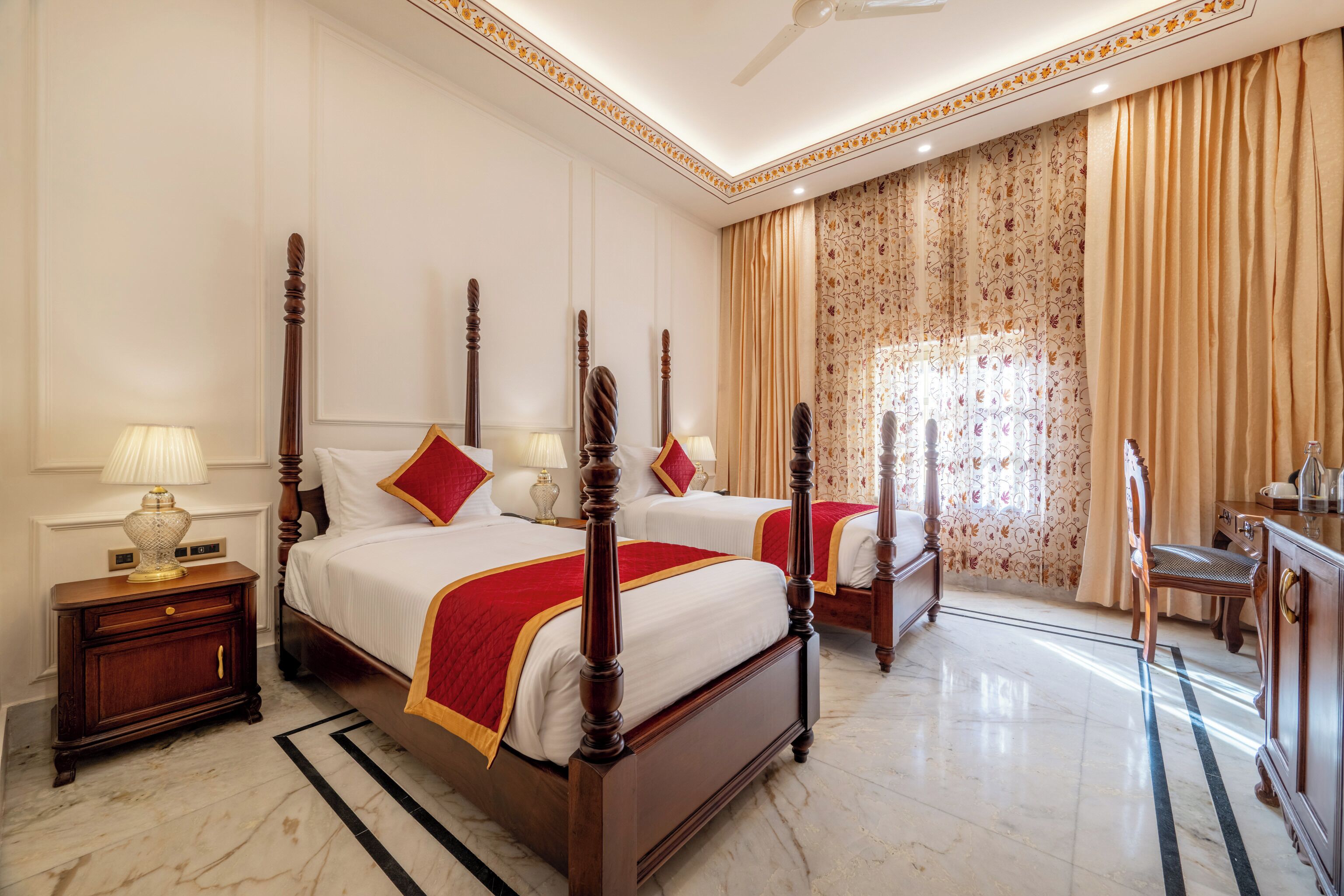 A hotel room with two beds, a desk, a chair, and a large window with curtains.