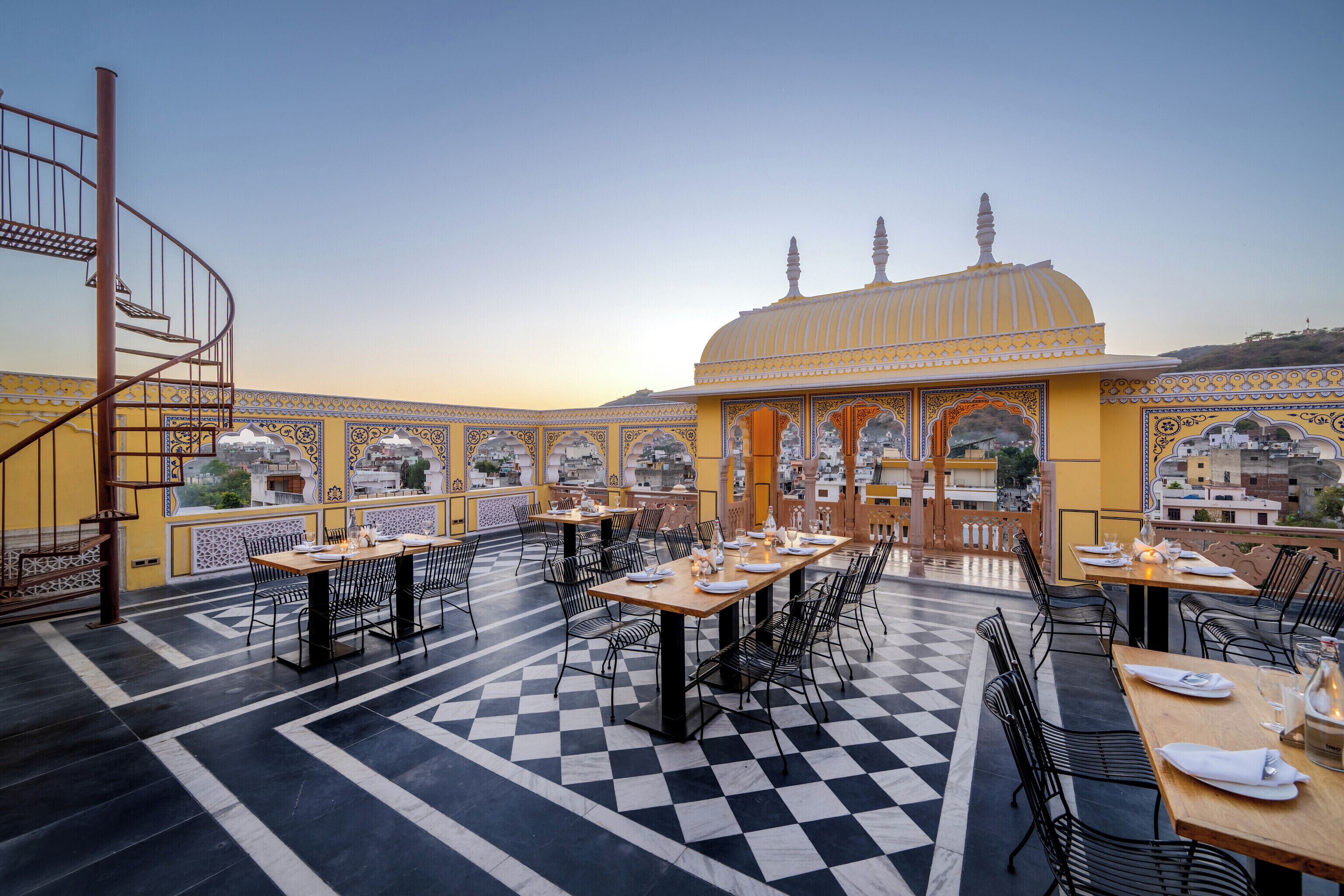 Un espace de restauration aménagé sur le toit, avec un sol à carreaux, des tables dressées et un bâtiment décoratif doté d’un dôme en arrière-plan.