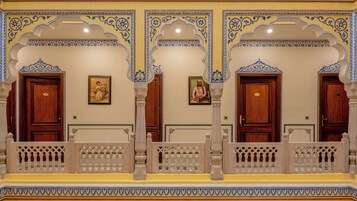Um corredor com azulejos azuis e brancos ricamente decorados, portas de madeira e uma varanda com grades detalhadas.