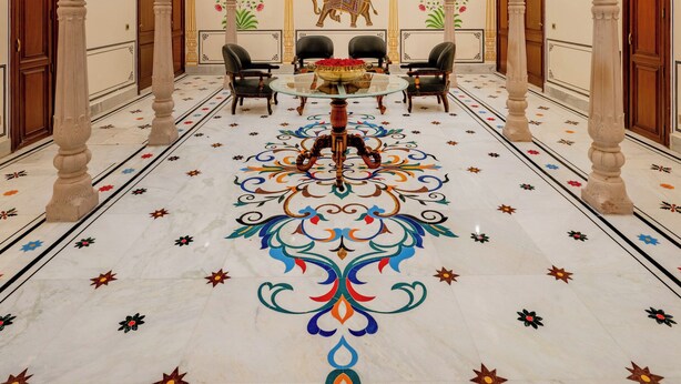 A grand hall with ornate columns, a central table, and a detailed floor design. - BRIJ CASTLE (Jaipur)