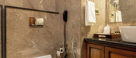 A modern bathroom with a marble wall, a white toilet, a wooden vanity, and a large mirror.