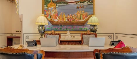 Una habitación con un escritorio, dos portátiles, una estatua y un cuadro de un paisaje fluvial.