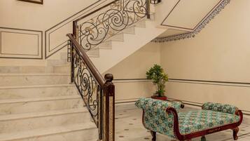 A marble staircase with ornate railings, a bench, and a potted plant.