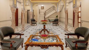 A grand hall with ornate columns, a central table with chairs, and a staircase leading to an upper level. - BRIJ CASTLE (Jaipur)